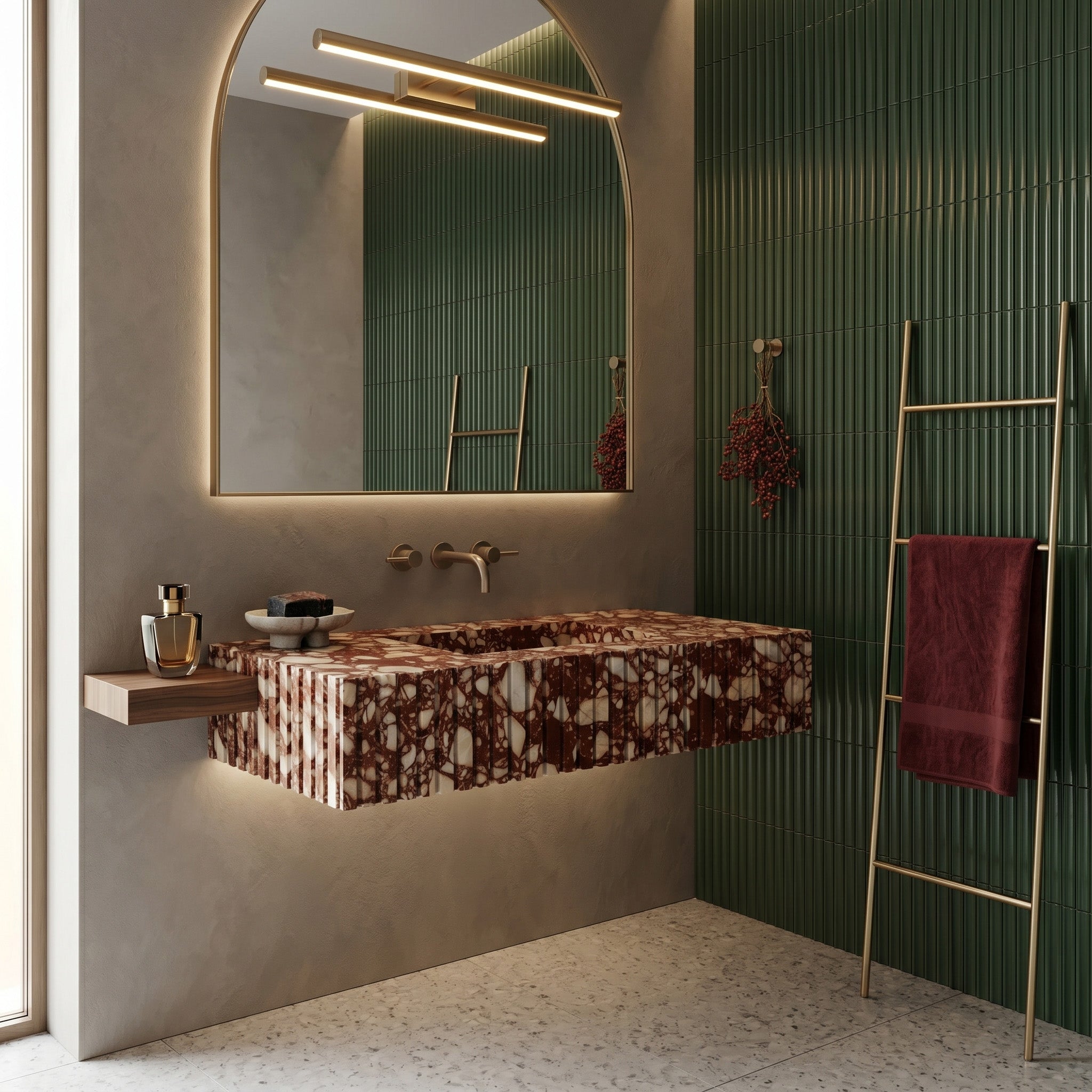 Modern luxury bathroom interior featuring a fluted red breccia marble single sink, a floating wooden side shelf, an arched backlit mirror, deep green kit kat wall tiles, and a brass towel ladder.