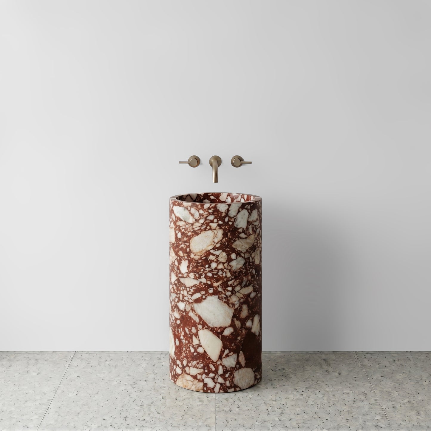 Front view of a solid Red Bulgari marble cylinder pedestal sink showcasing bold crimson brecciation with wall-mounted bronze tapware.
