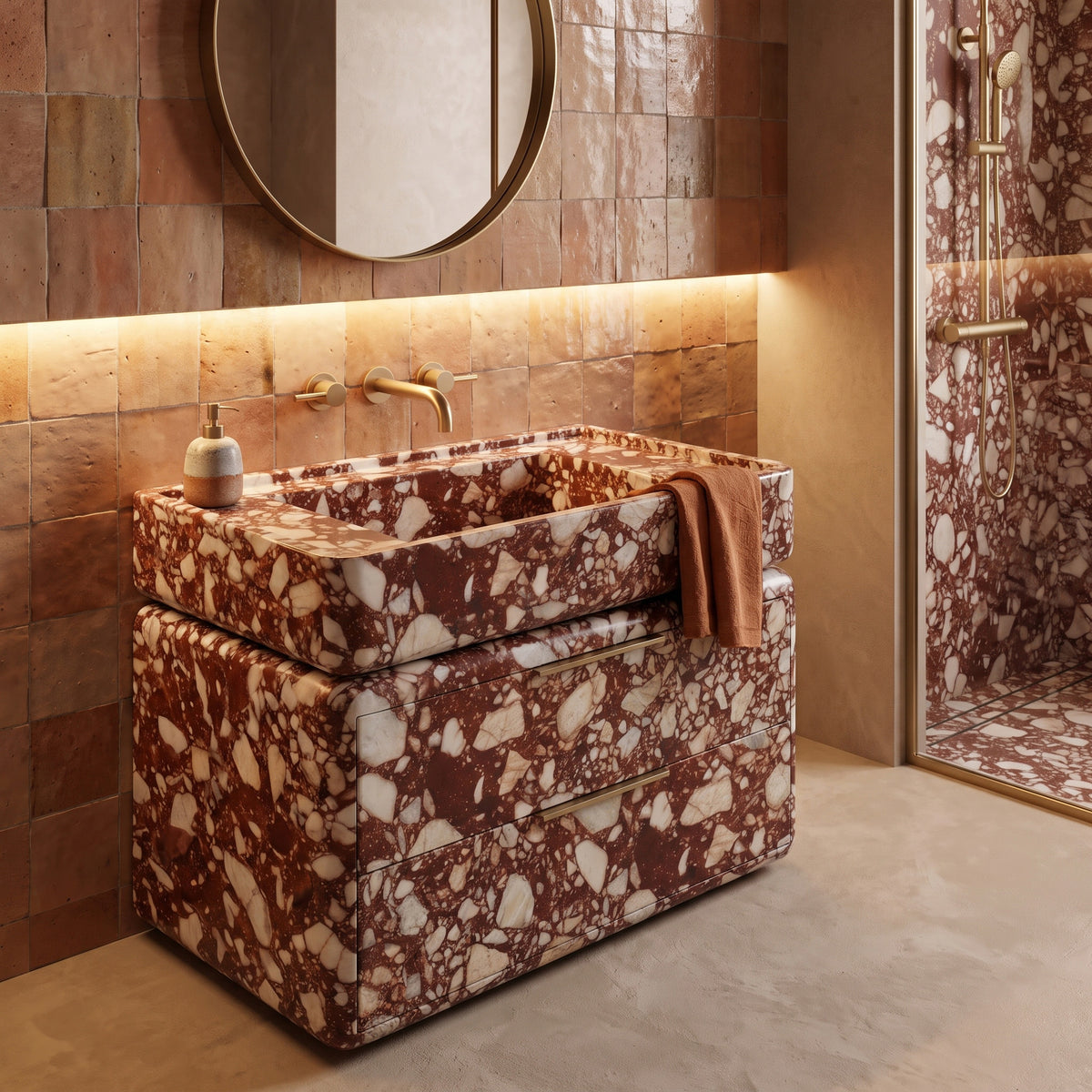 Warm Mediterranean luxury bathroom interior featuring the curved Red Bulgari marble double-drawer vanity draped with a rust hand towel, paired with wall-mounted brass tapware, a backlit round mirror, earthy terracotta square wall tiles, and a matching stone shower enclosure.
