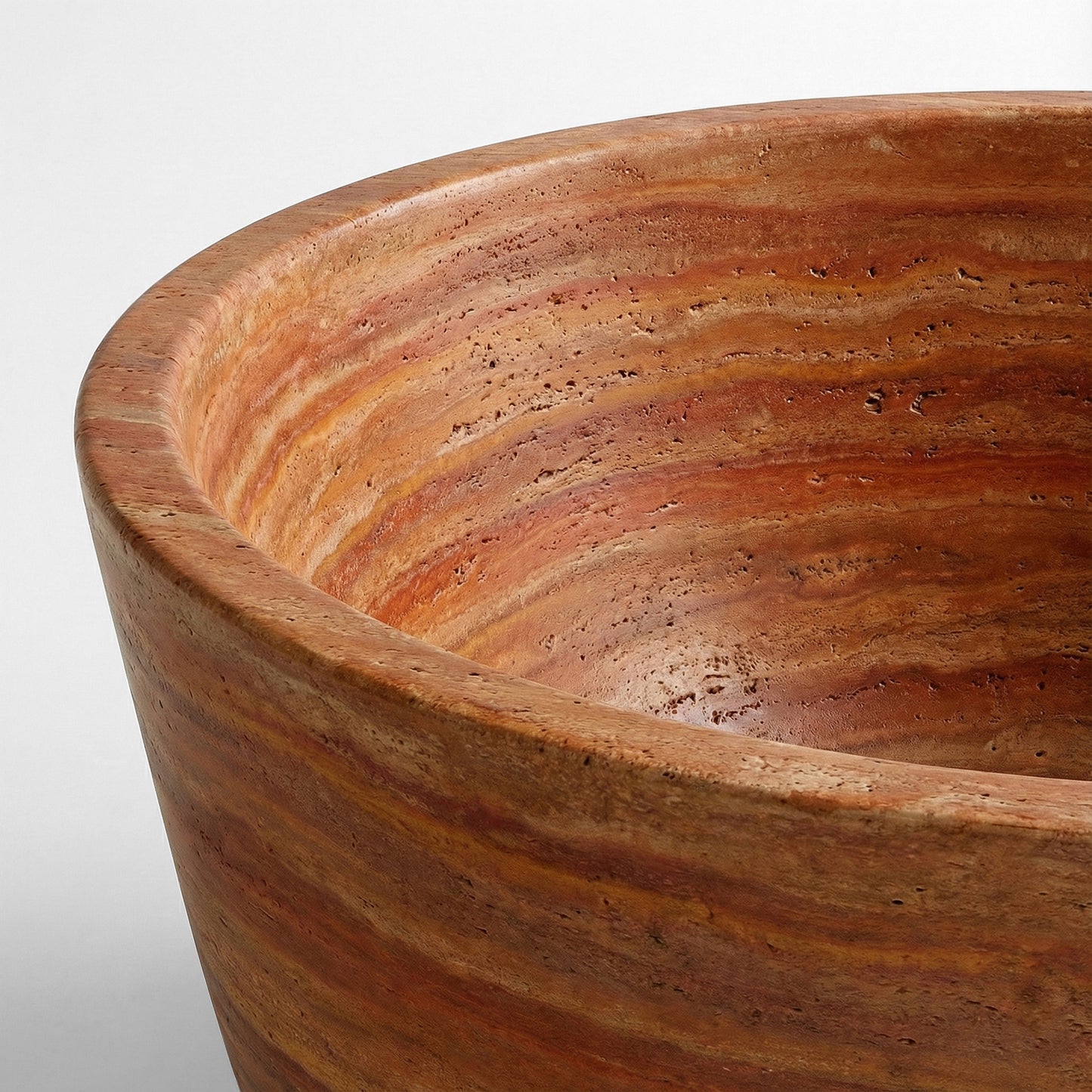 Close-up macro shot of a Red Travertine bathtub rim showing the raw, porous texture and vibrant sedimentary layers of the natural stone.