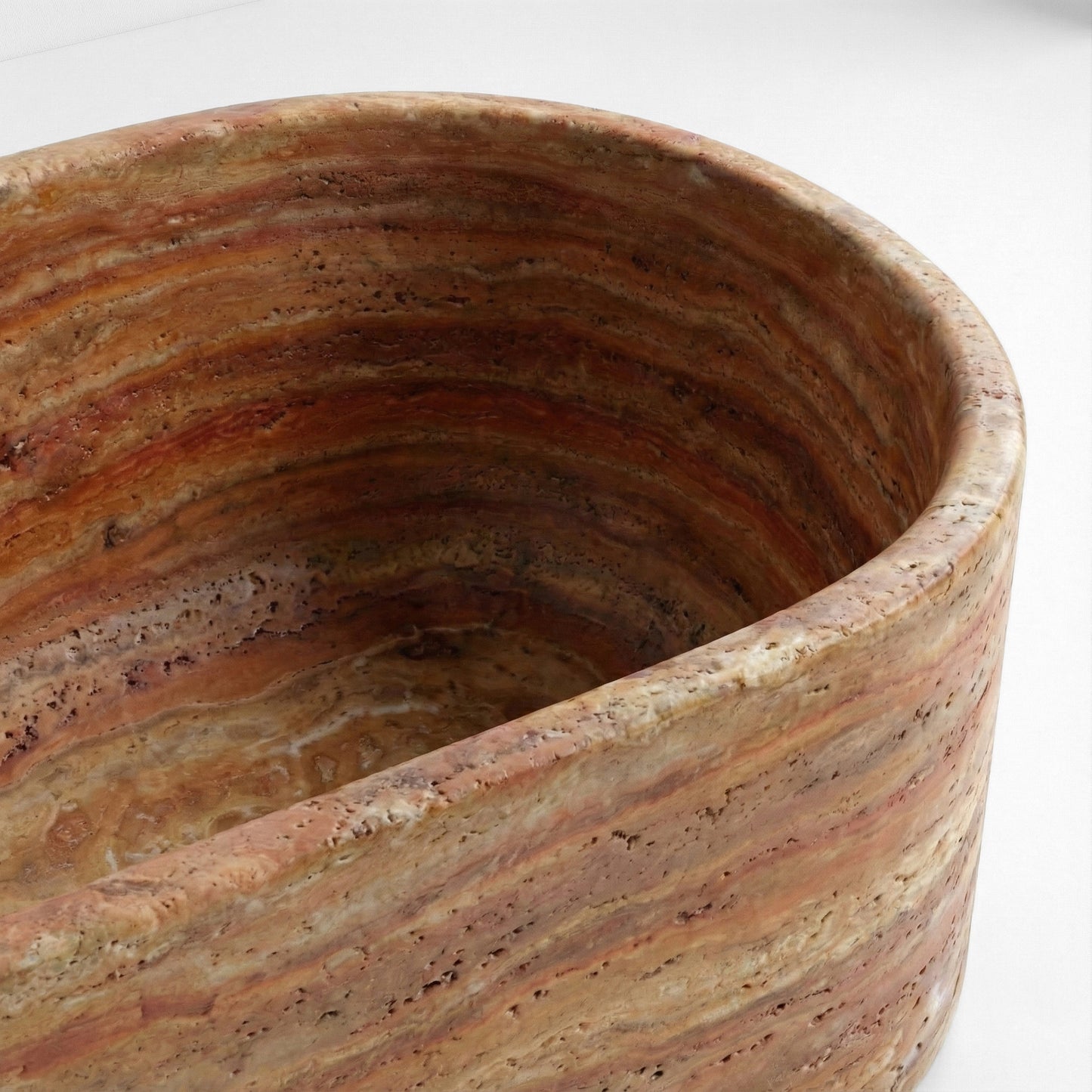 Close-up detail of a Red Travertine bathtub rim highlighting the porous texture and rich terracotta mineral banding.