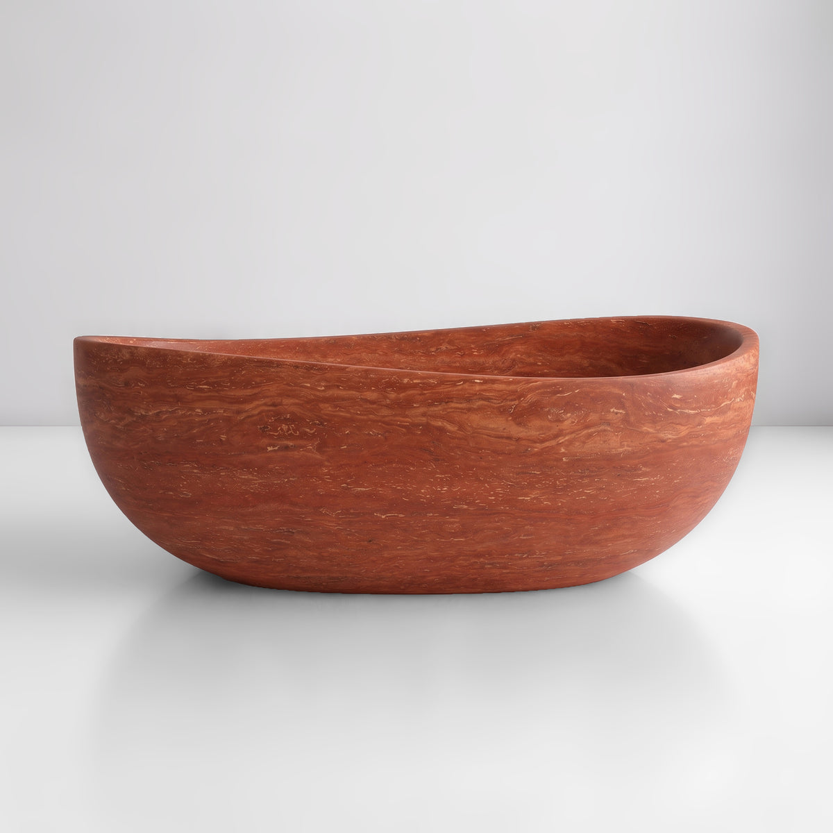 Front studio view of the freestanding Red Travertine wave bathtub, showcasing the organic dipping rim silhouette and warm terracotta, rust, and clay horizontal sedimentary strata across the stone exterior.