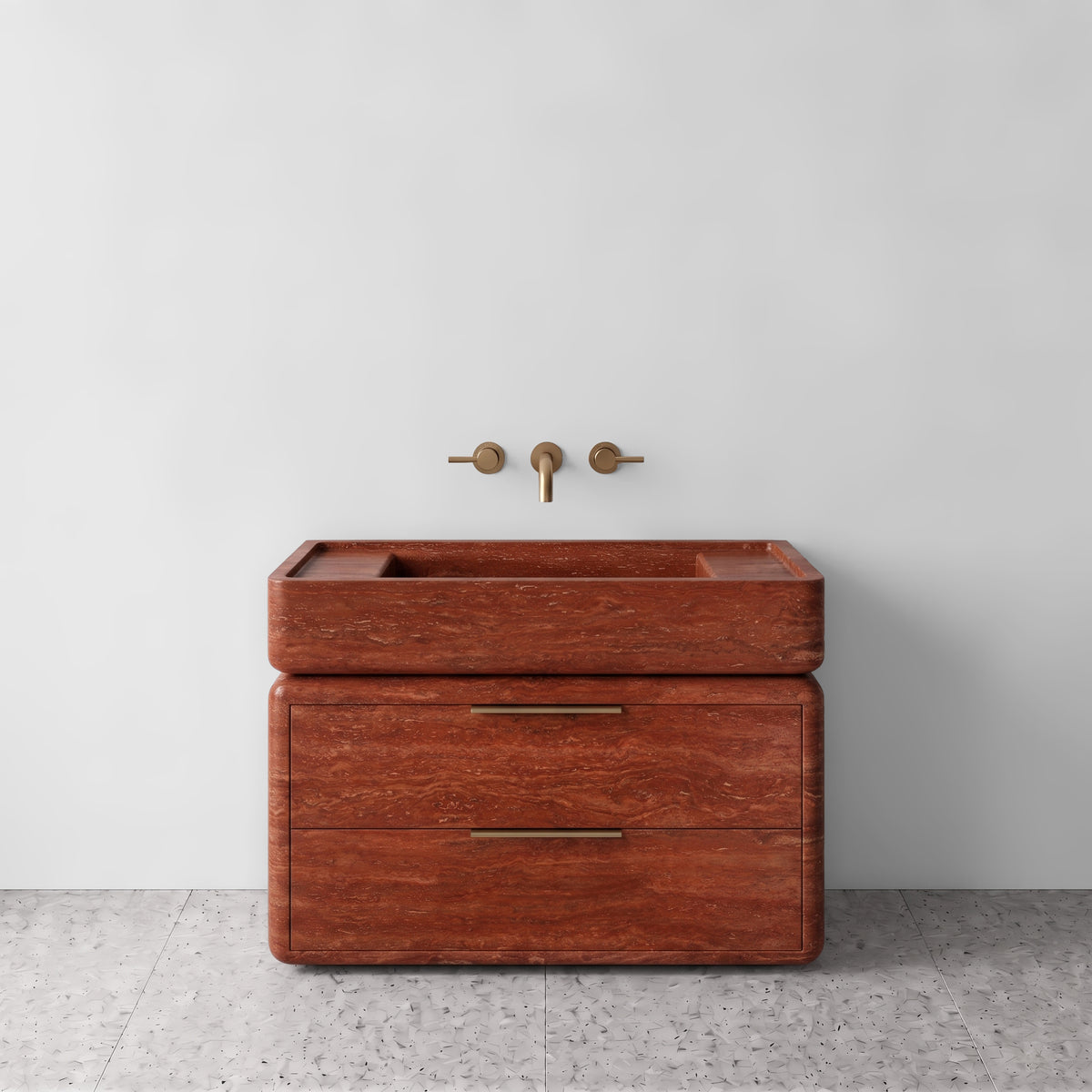 Front studio view of the freestanding Red Travertine double-drawer vanity, featuring rounded corners, an integrated trough basin, horizontal brushed brass pulls, and wall-mounted three-hole brass tapware set against a white wall and terrazzo flooring.