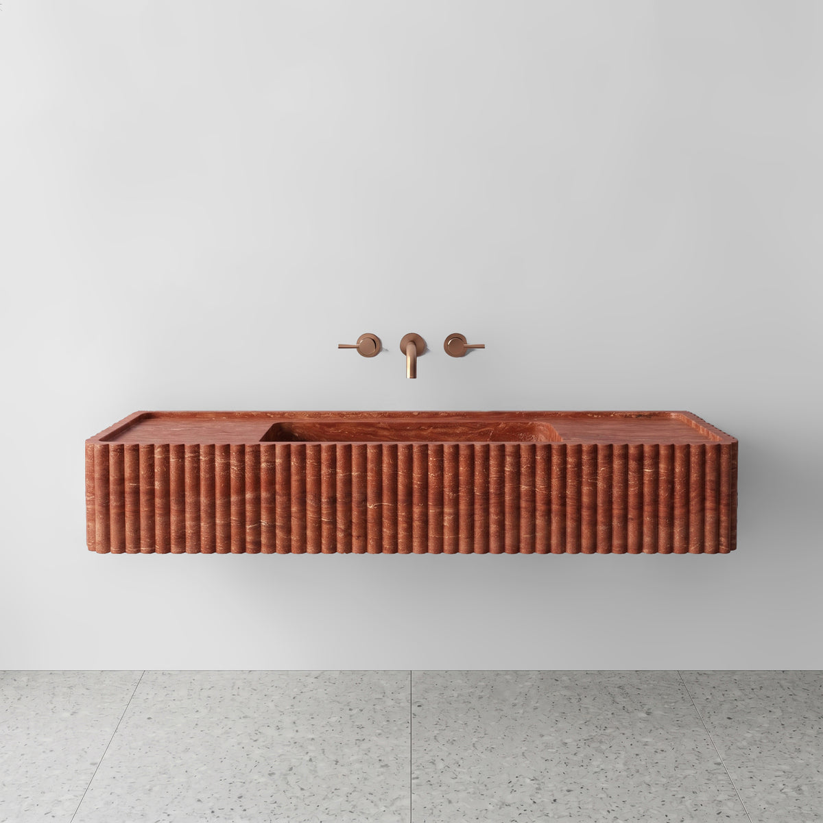 Front view of the Red Travertine fluted monolith sink showing rich terracotta and rust sedimentary banding across the vertical convex ribbed apron and wall-mounted brushed bronze tapware.