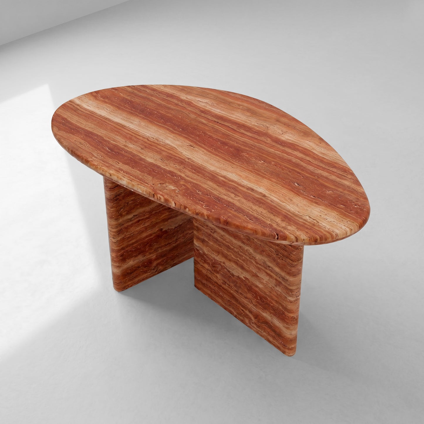 High-angle view of a pebble-shaped red travertine coffee table displaying its unique organic silhouette and rich, earthy natural stone patterns.