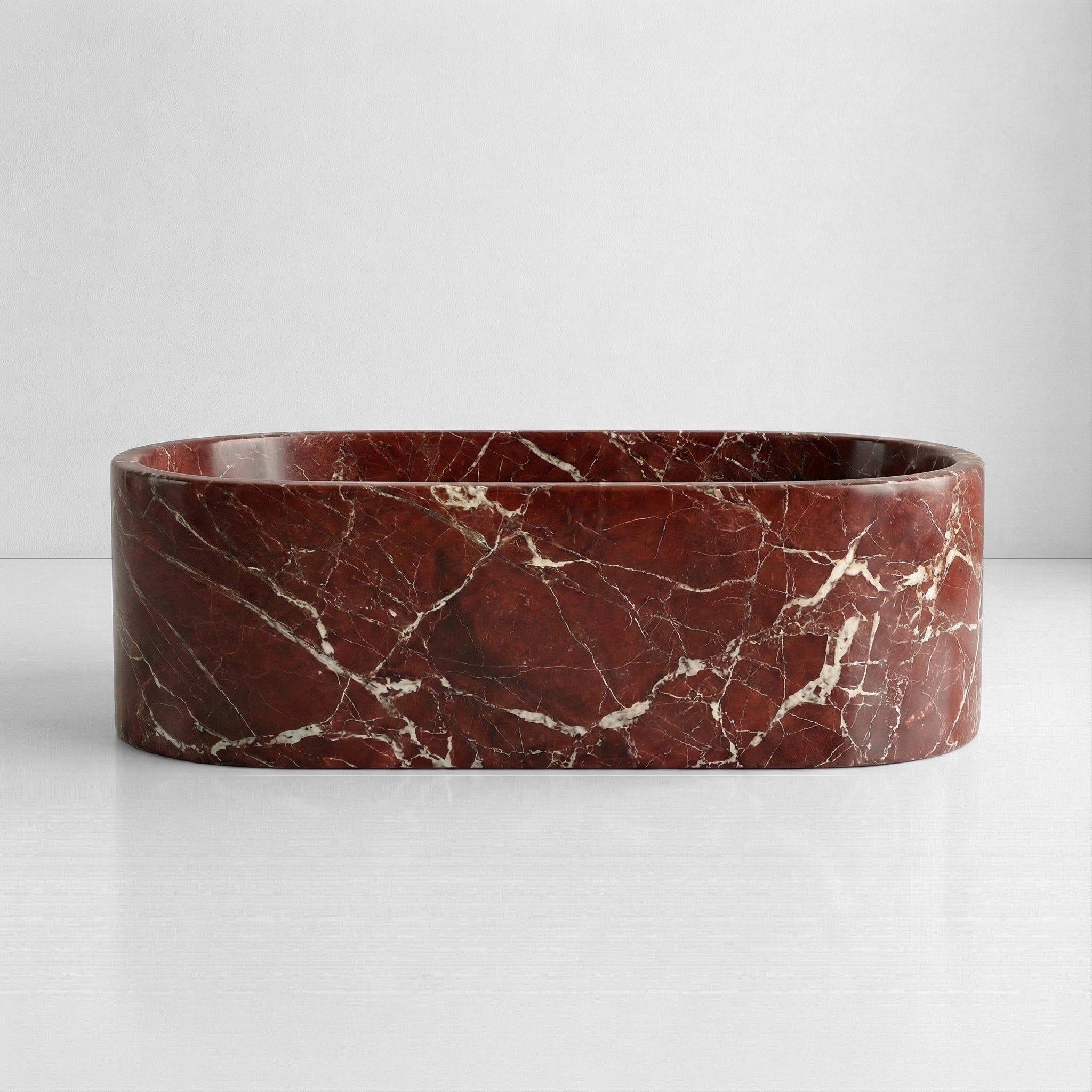 Front elevation of a solid oval bathtub carved from Rosso Levanto marble, displaying a dramatic contrast between the dark red surface and white veins.