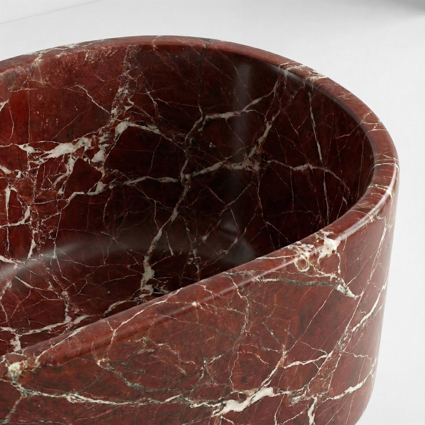 Close-up detail of a Rosso Levanto marble bathtub rim highlighting the rich wine-colored background and spiderweb-like white mineral patterns.