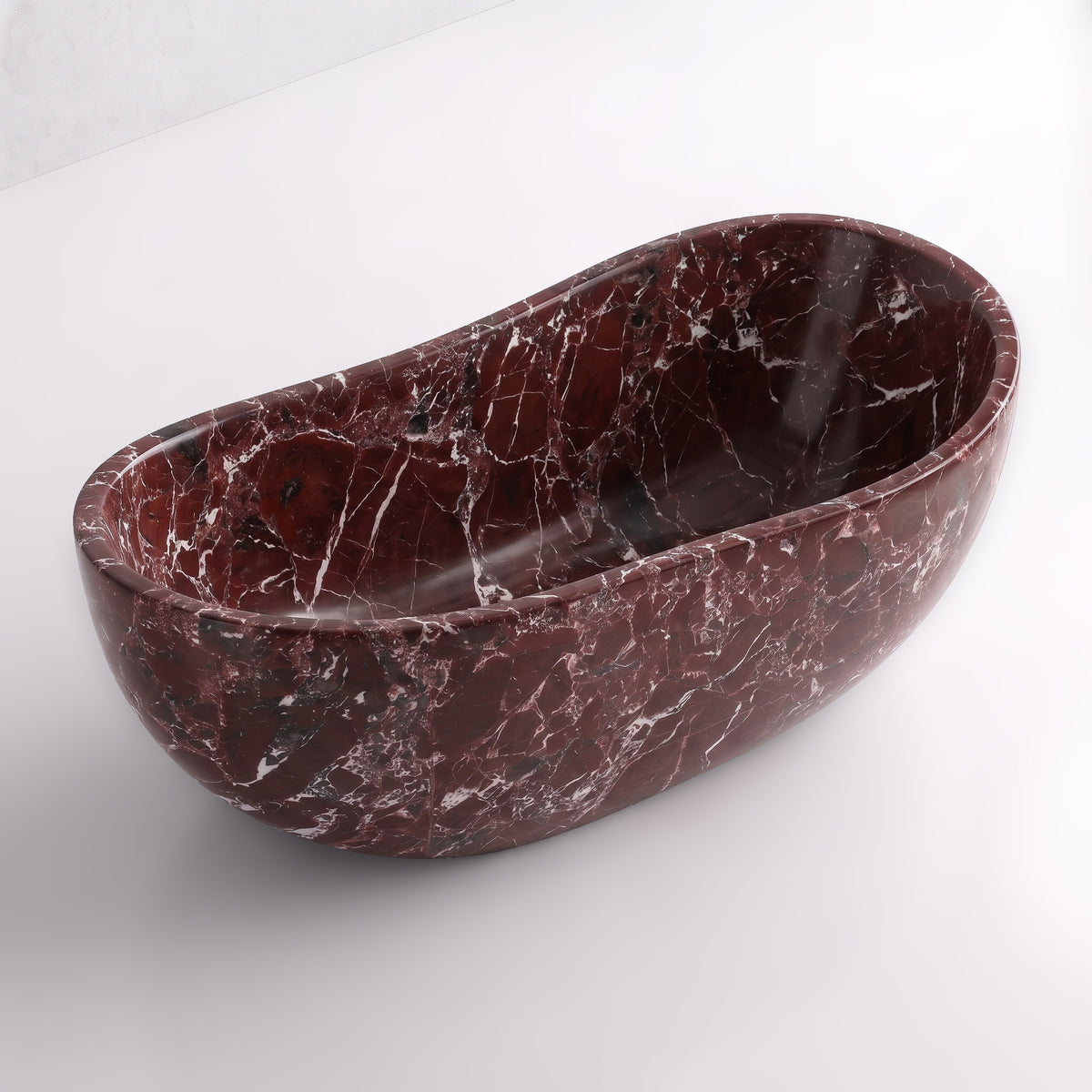 Elevated three-quarter perspective view of the Rosso Levanto marble wave soaking tub, highlighting the asymmetrical undulating rim, seamless solid-carved interior, and striking white spiderweb veining across rich burgundy stone.