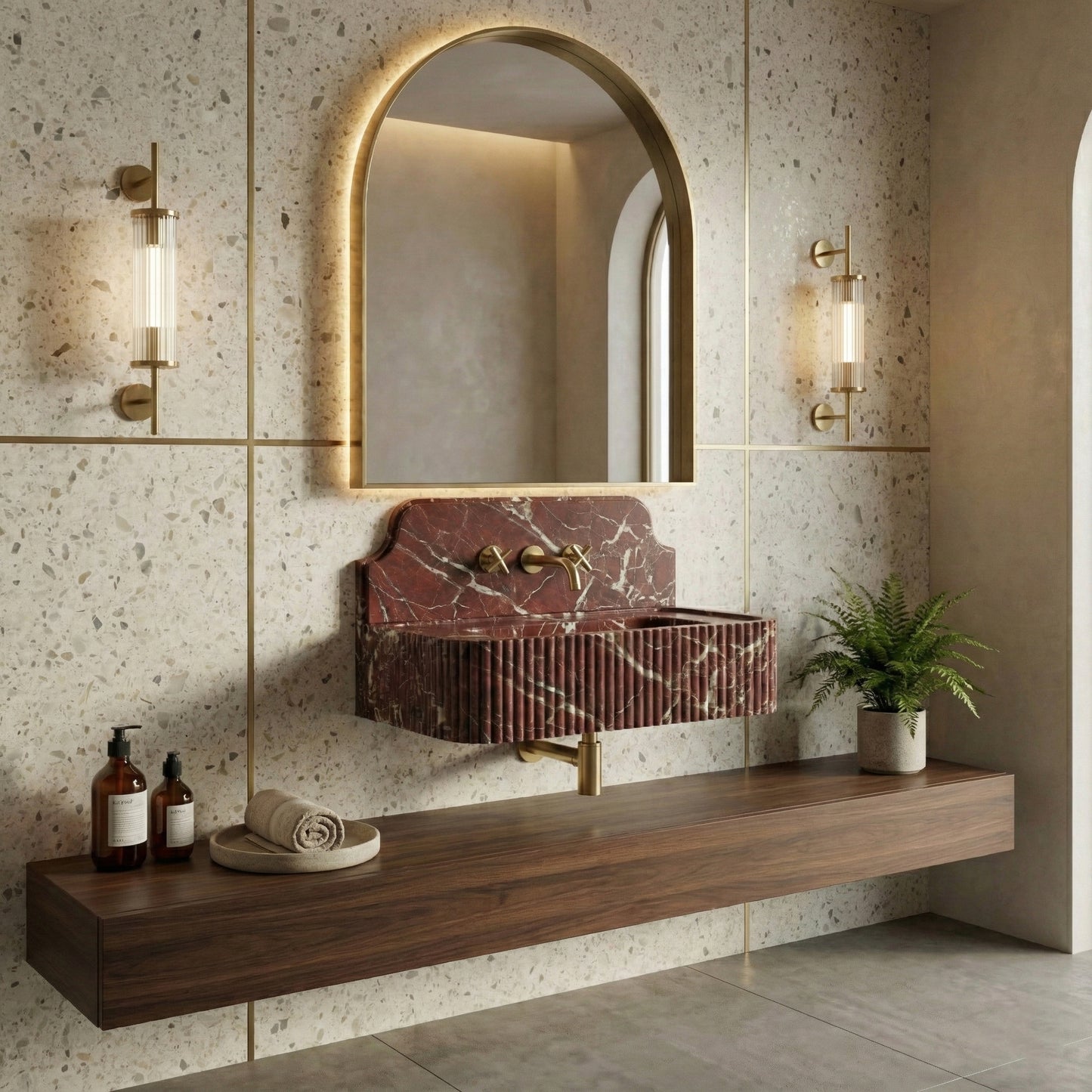 Classic luxury powder room featuring a Rosso Levanto marble sink with backsplash, mounted against terrazzo tiled walls with brass sconces and an arched mirror.