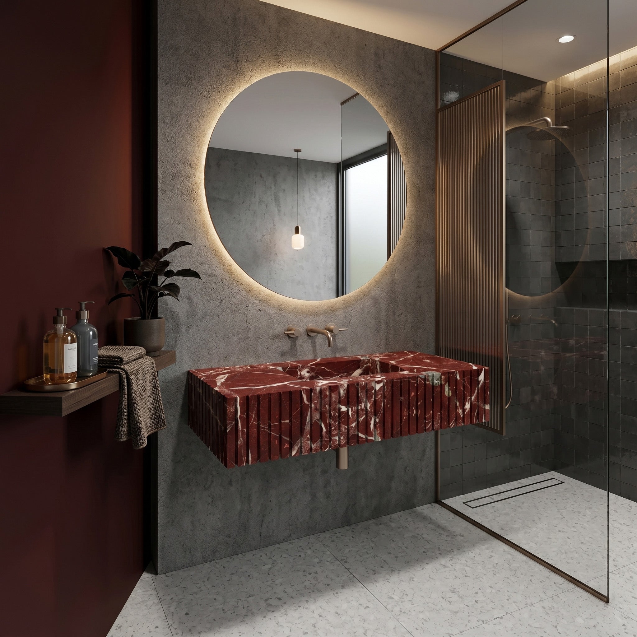 Moody luxury bathroom interior featuring a fluted red Rosso Levanto marble single sink, a large backlit round mirror, textured raw concrete walls, a reeded brass shower screen, and a dark burgundy accent wall.
