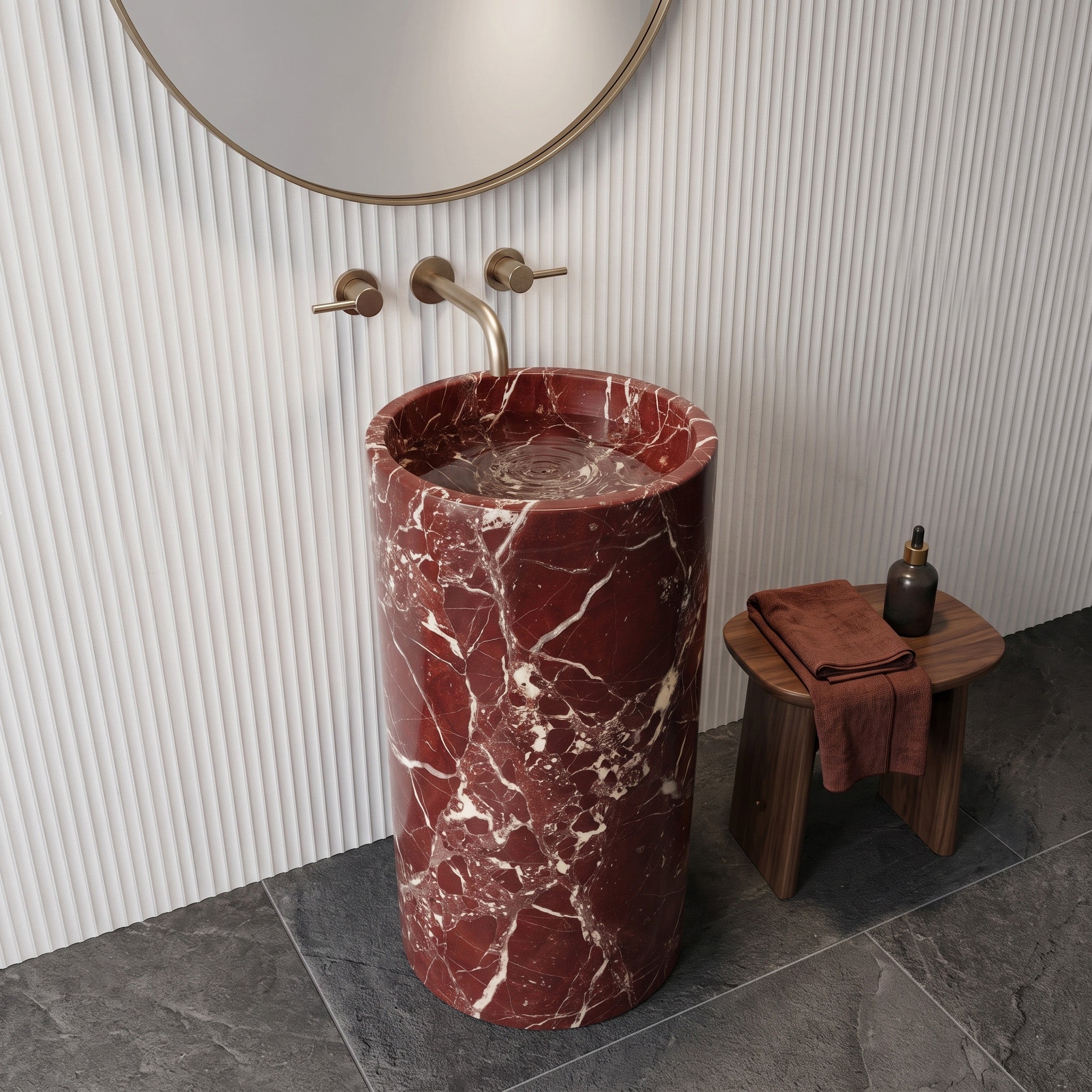 Freestanding Rosso Levanto marble round pedestal basin in a modern luxury bathroom with fluted white wall paneling, charcoal slate tiles, and round brass mirror.