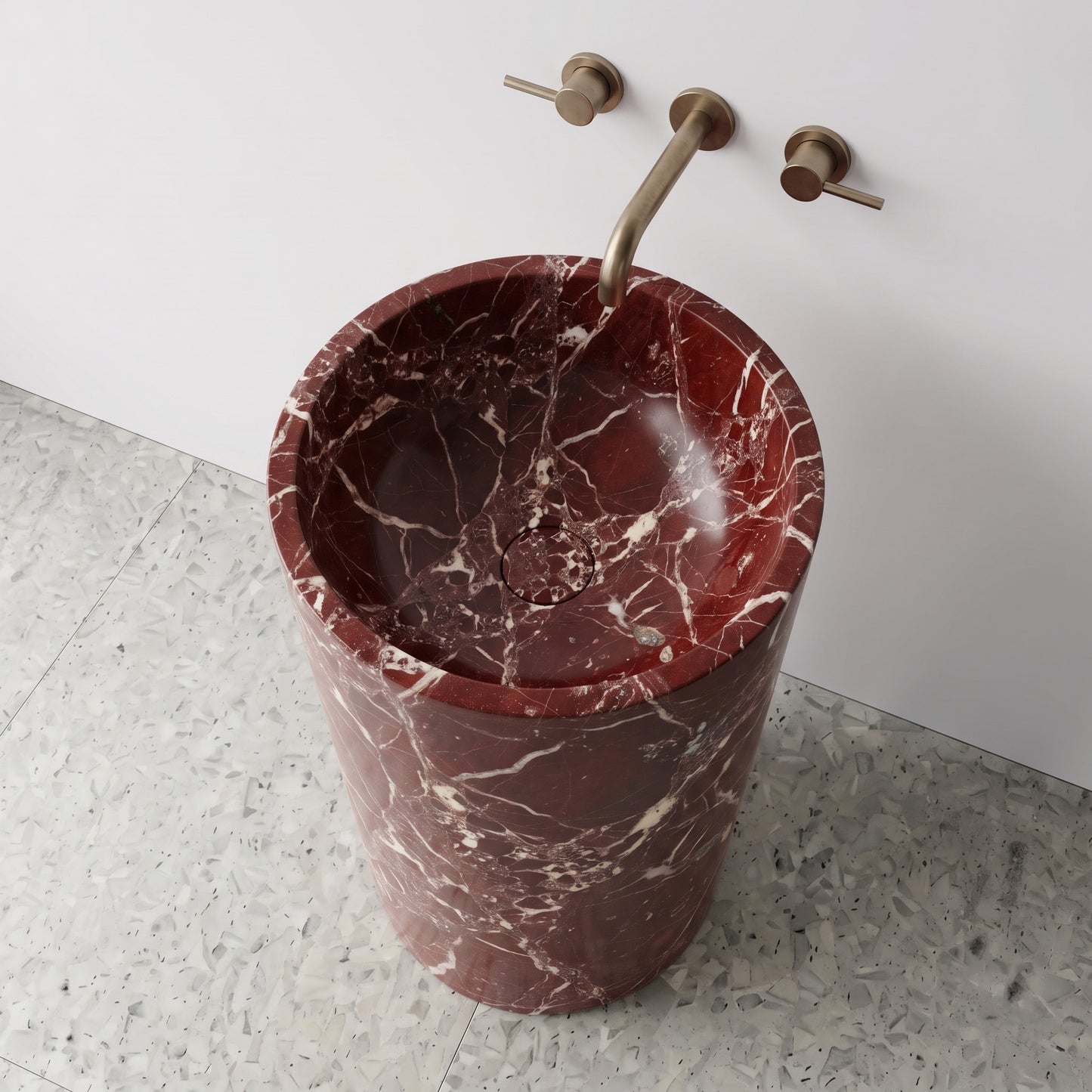 High-angle top view of a solid Rosso Levanto cylindrical marble pedestal sink highlighting vivid white calcite veining on deep cherry stone with matching drain cover.