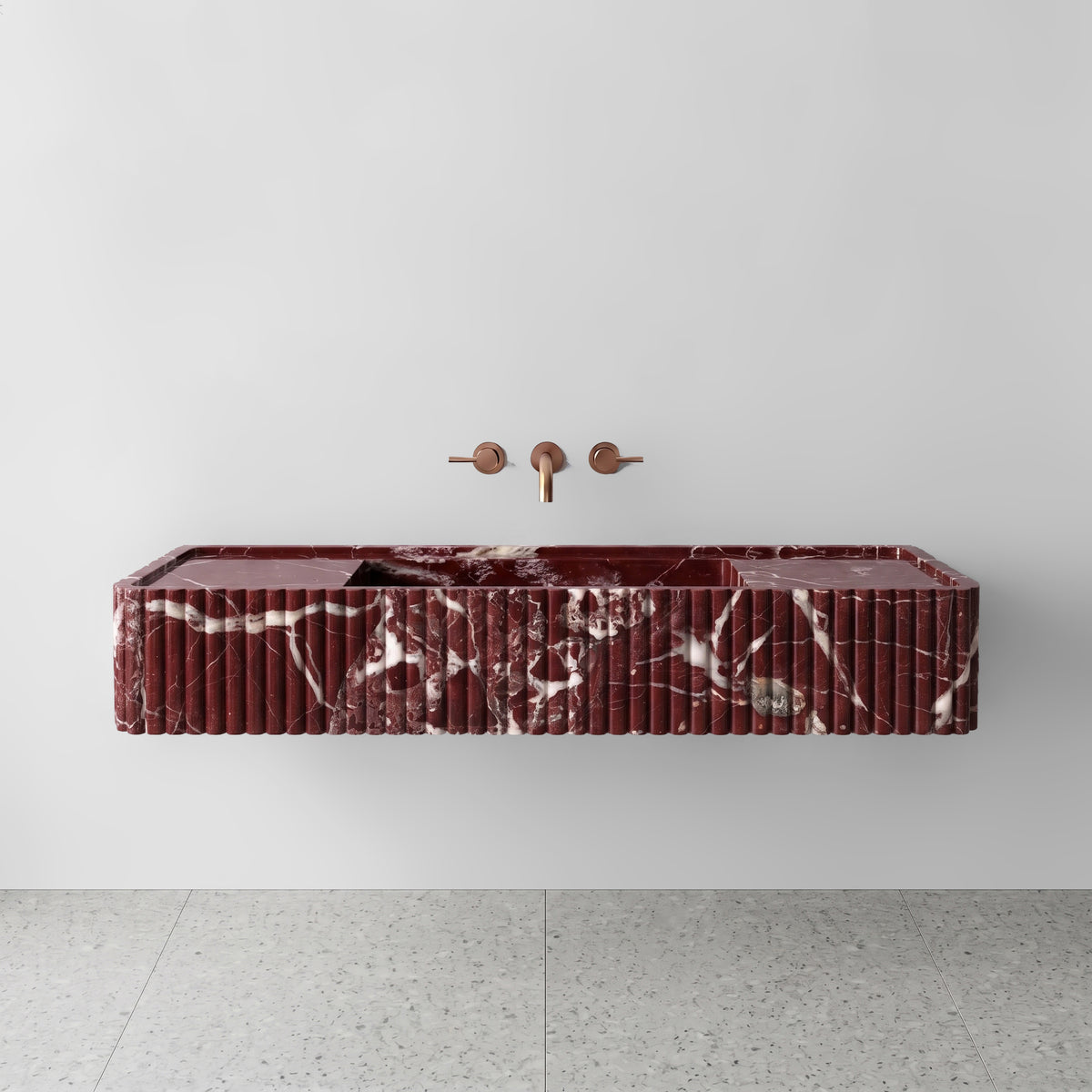 Front view of the Rosso Levanto marble fluted monolith sink showing rich wine-red tones and crisp white calcite veining across the vertical convex ribbed apron and wall-mounted brushed bronze faucet.