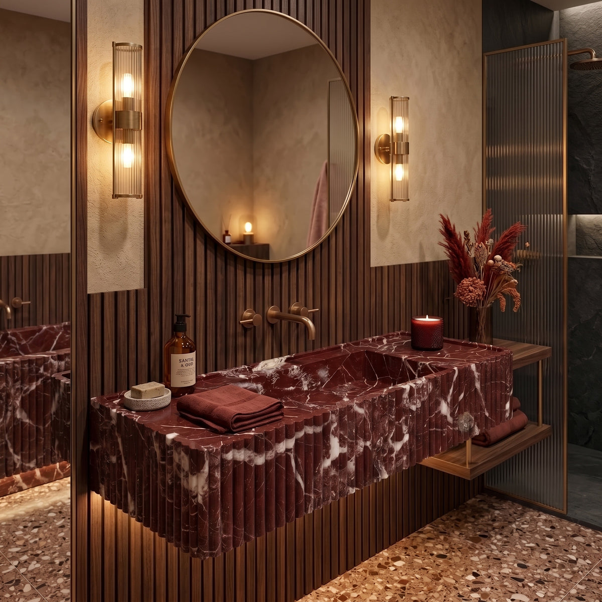 Atmospheric luxury bathroom interior featuring the floating Rosso Levanto fluted stone vanity set against vertical fluted walnut wall panels, a circular bronze mirror, and amber terrazzo flooring.