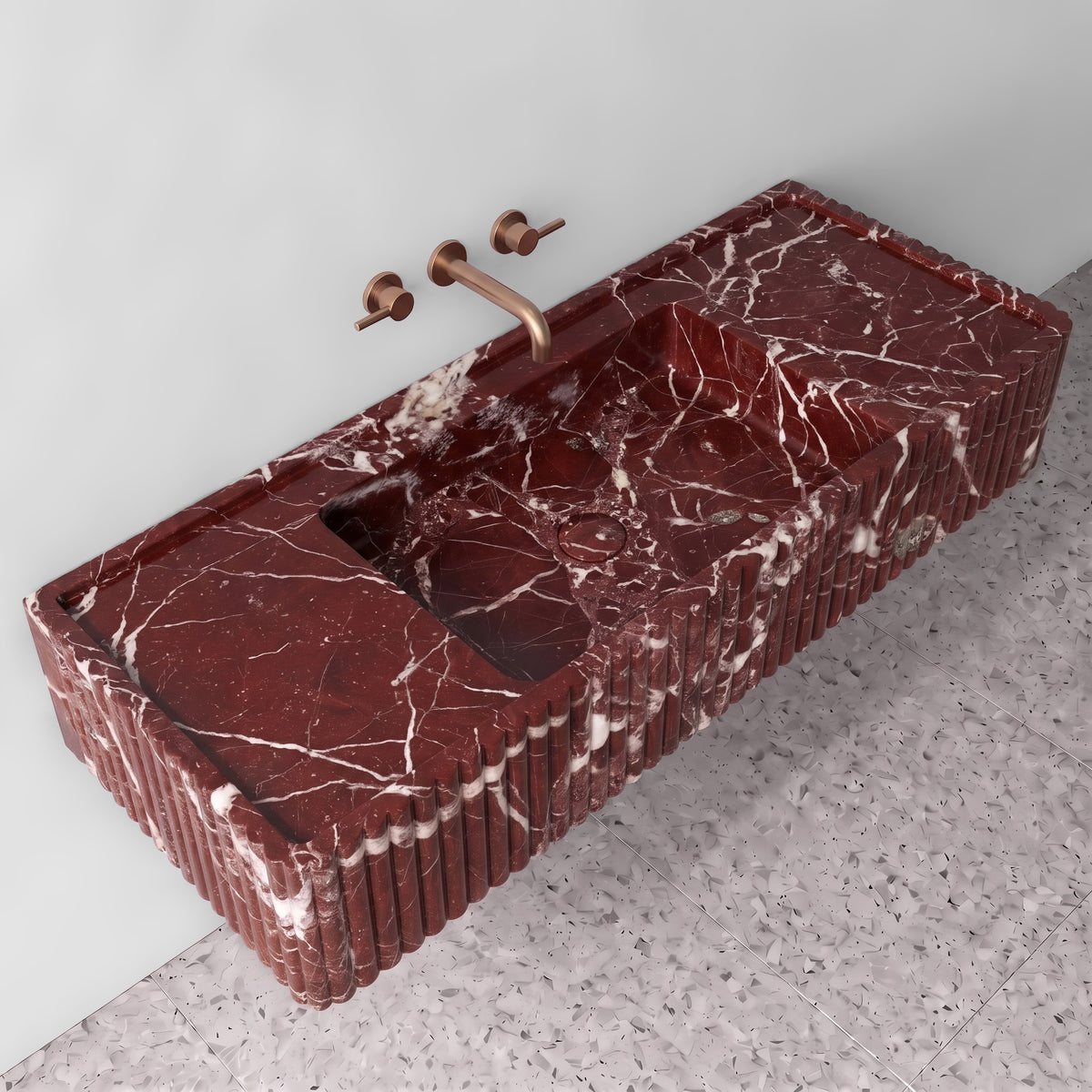 Elevated three-quarter angle of the Rosso Levanto fluted monolith sink showing the integrated trough basin, matching stone drain cover, raised perimeter edge, and ribbed side detailing.