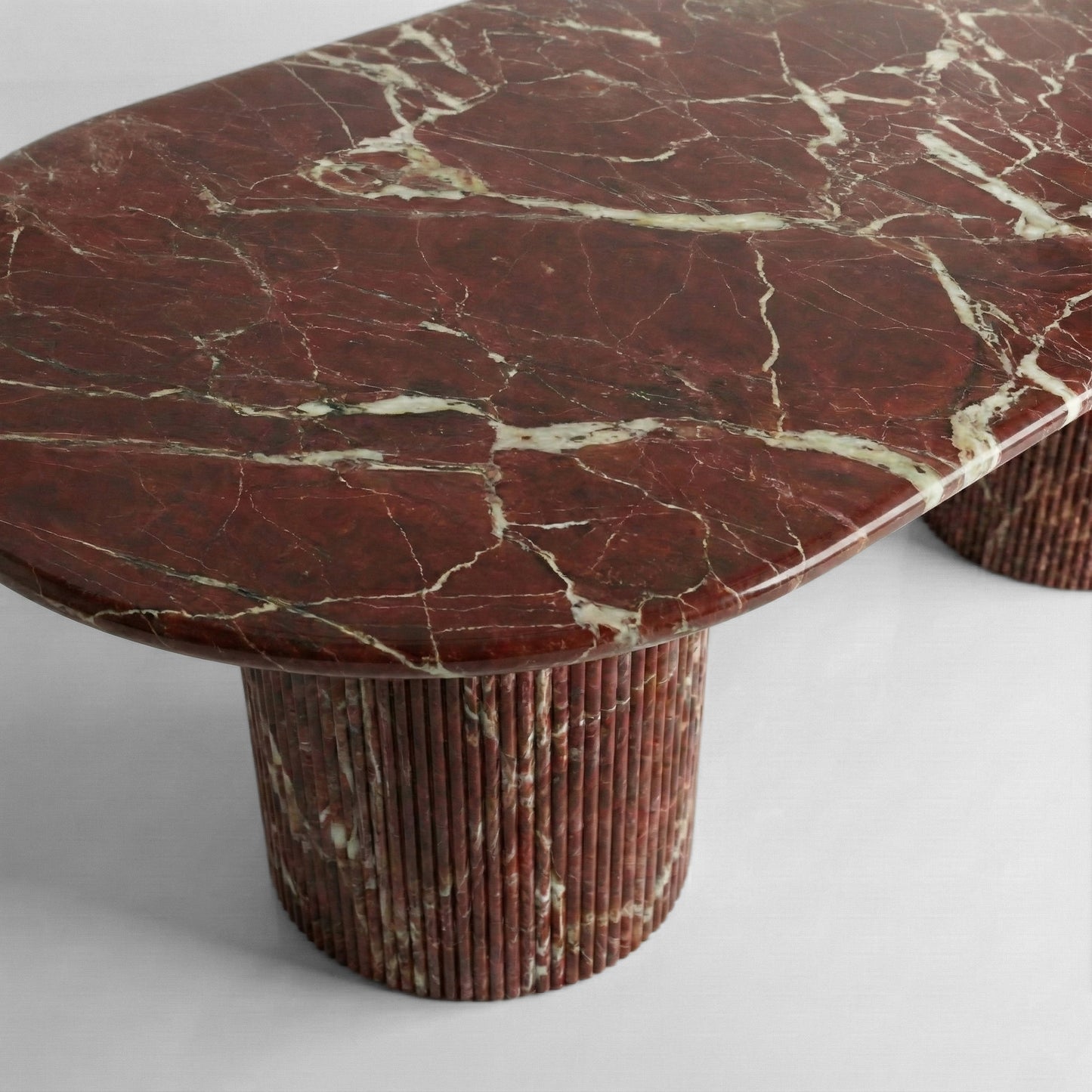 Side profile of a Rosso Levanto marble dining table showing the thick polished stone top and dual ribbed pedestal legs in a rich dark red hue.