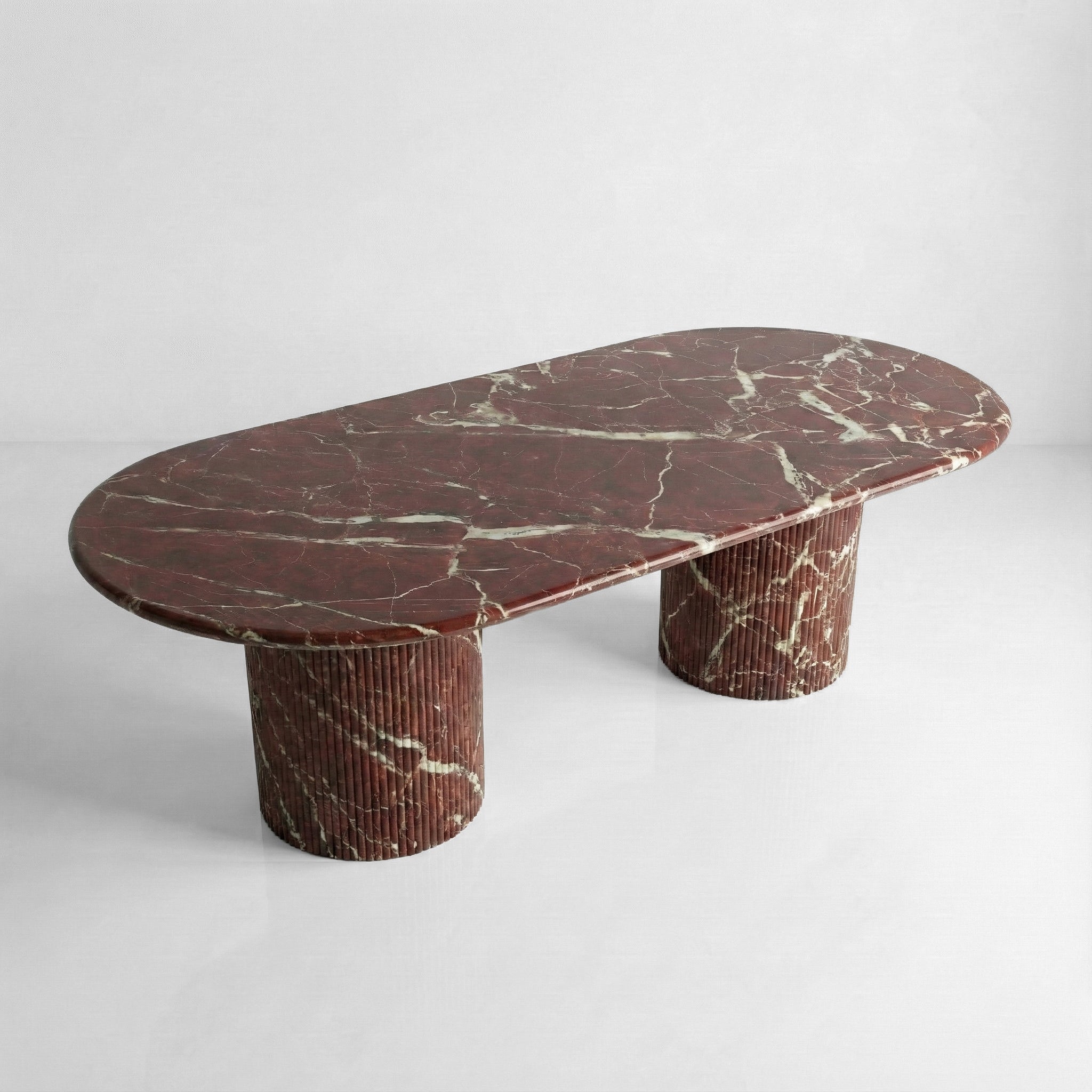 High-angle view of a large oval Rosso Levanto marble dining table, showcasing the deep wine-red stone surface with striking white lightning veins.