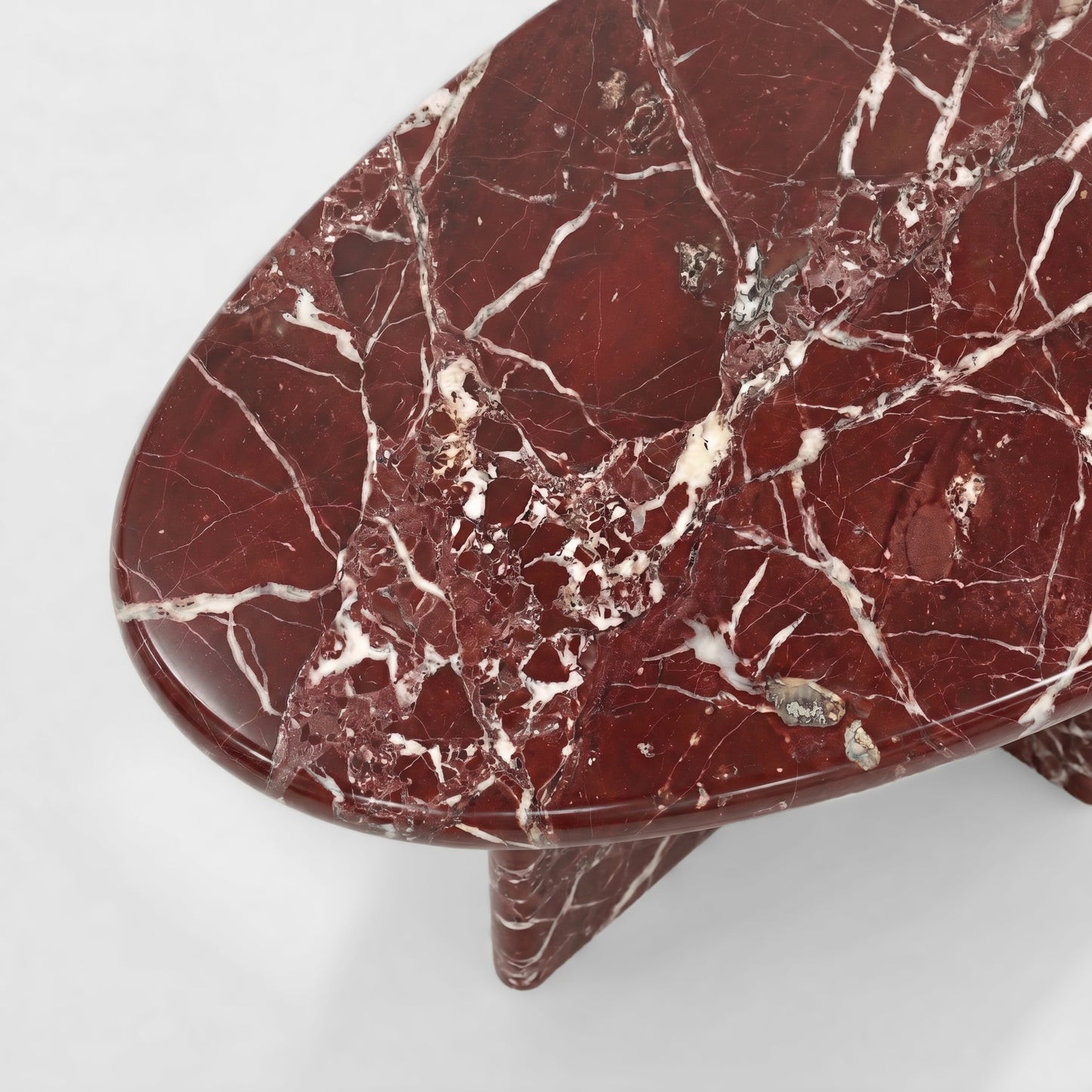 Side profile of a bespoke Rosso Levanto marble coffee table featuring a sculptural two-pedestal base and a thick pebble-shaped top against a minimalist white background.