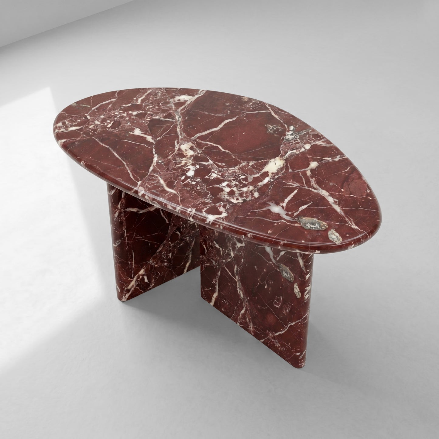 High-angle top view of a pebble-shaped coffee table crafted from Rosso Levanto marble, displaying its unique organic silhouette and rich natural stone patterns.
