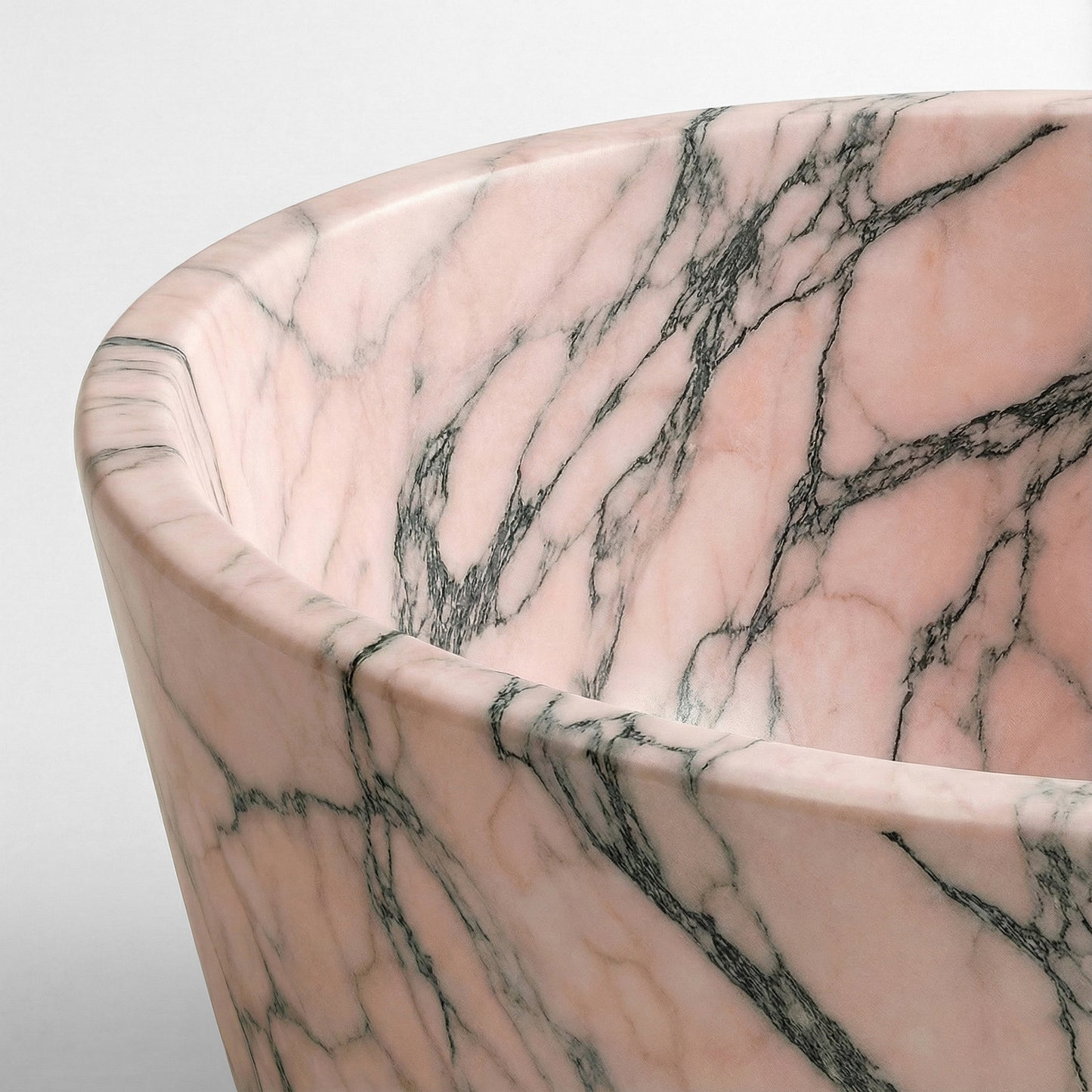 Close-up detail of a Rosso Portogallo bathtub rim highlighting the pastel salmon-pink hues and intricate dark grey natural stone patterns.