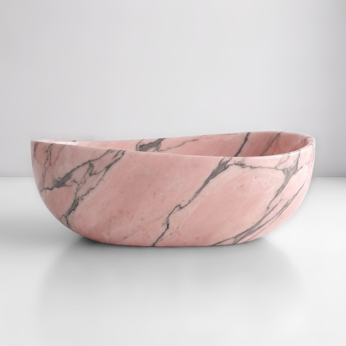Front studio view of the freestanding Rosso Portogallo marble wave bathtub, showcasing the organic dipping rim silhouette and soft salmon-pink ground with dark grey veining across the polished stone exterior.