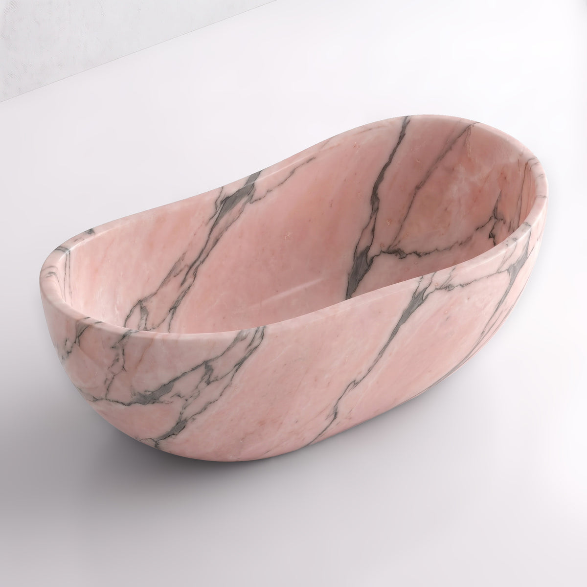Elevated three-quarter perspective view of the Rosso Portogallo marble wave soaking tub, highlighting the asymmetrical undulating rim, seamless solid-carved interior, and flowing charcoal-grey veining across blush-pink stone.