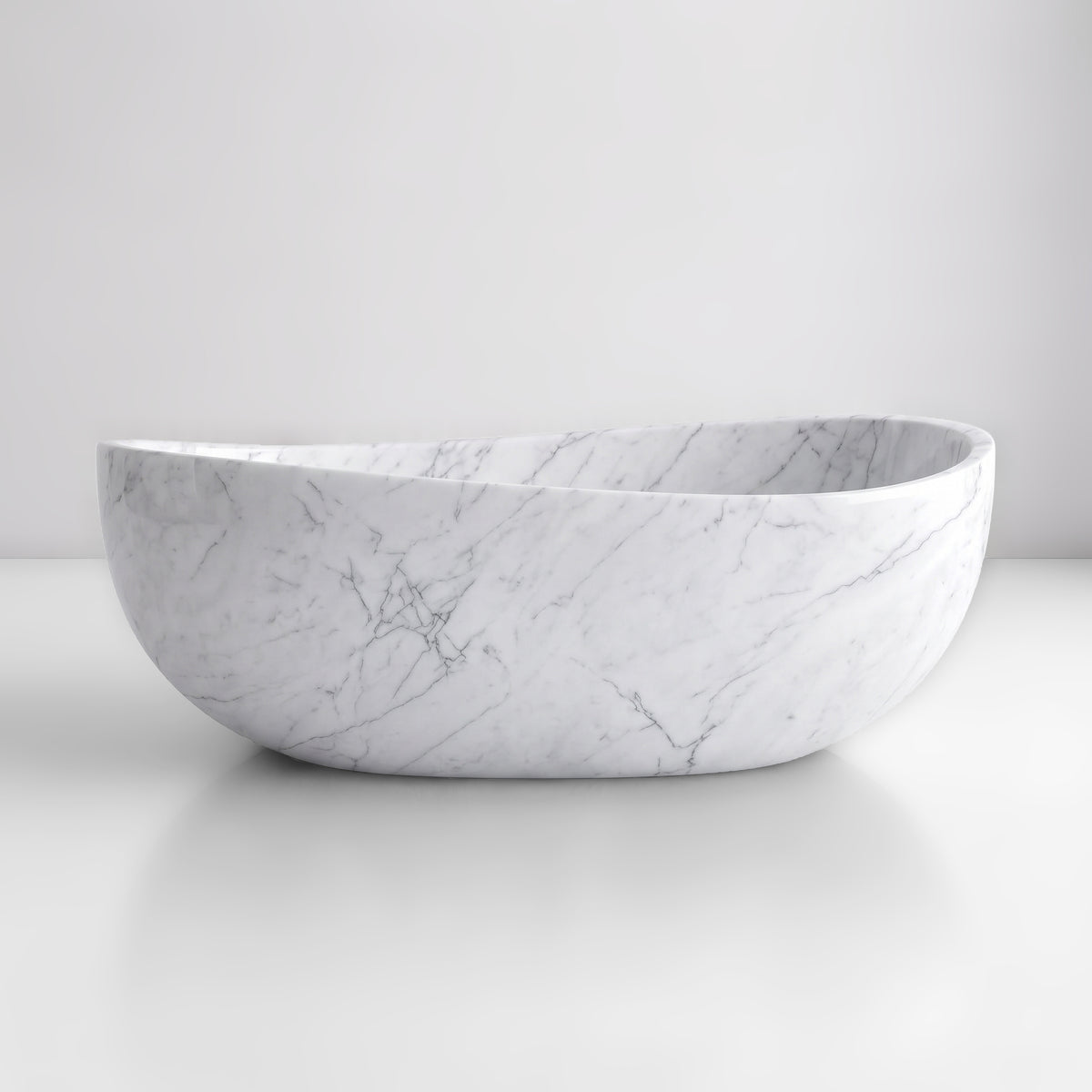 Front studio view of the freestanding White Carrara marble wave bathtub, showcasing the organic dipping rim silhouette and soft feathery smoke-grey veining across the cool off-white stone exterior.
