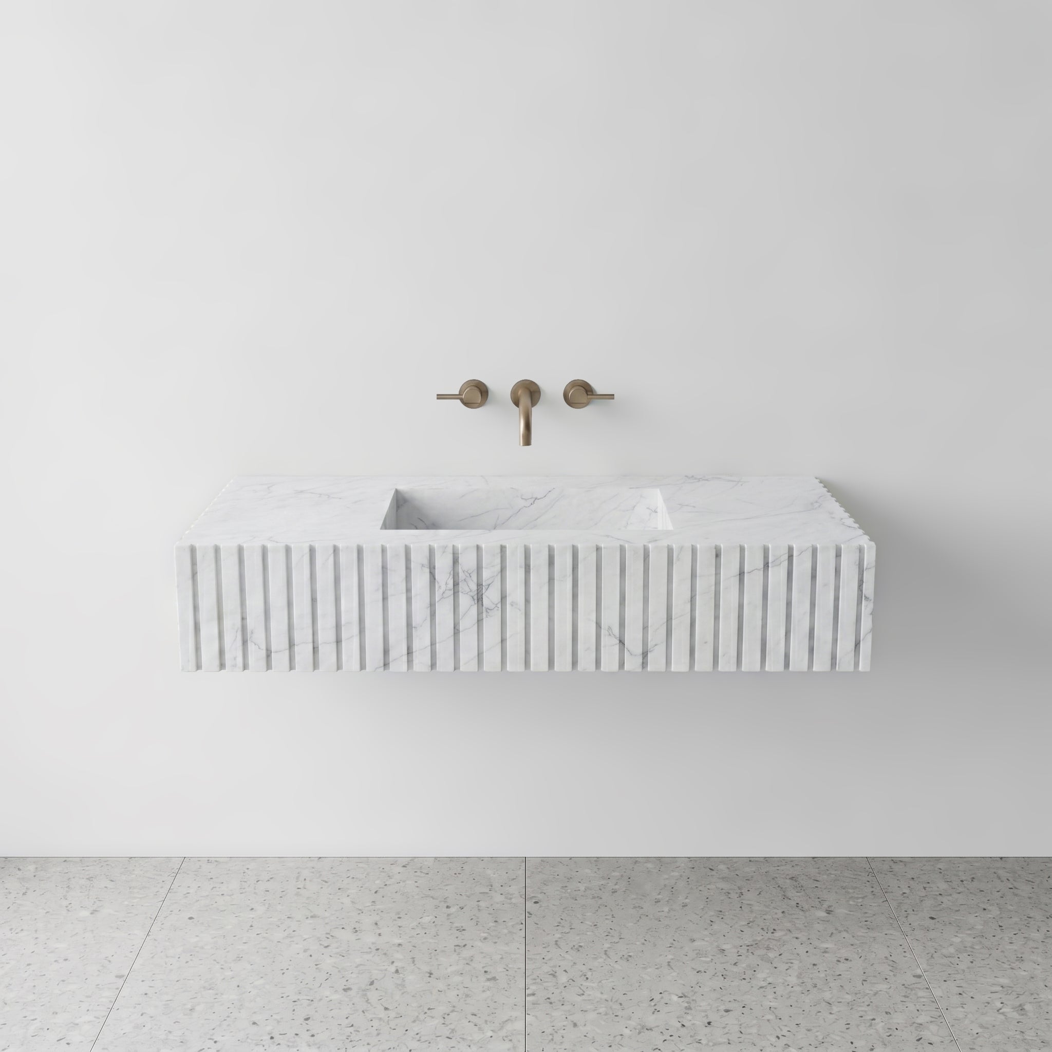 Front studio view of a luxury floating single sink vanity made of classic White Carrara marble, featuring a precision fluted apron front design and a wall-mounted brushed bronze faucet.