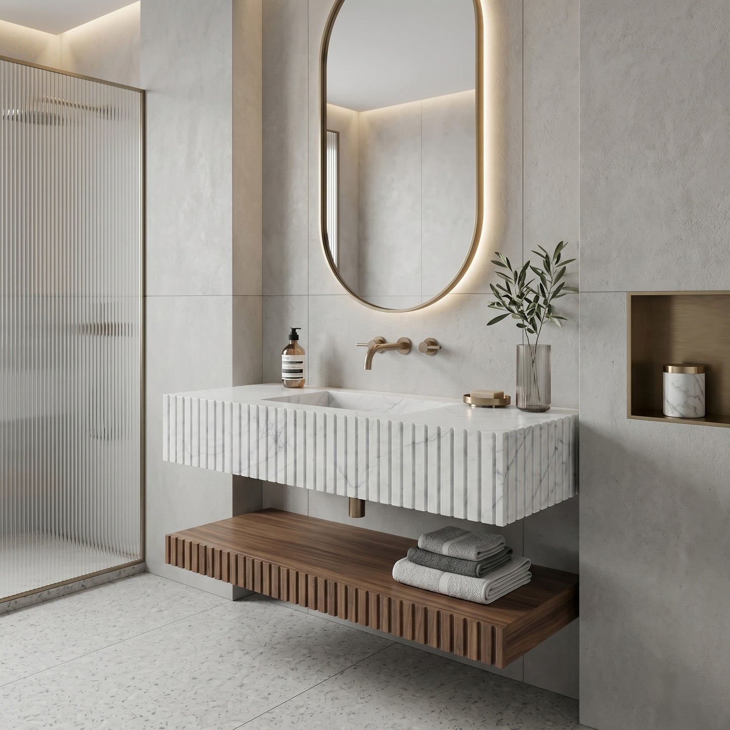 Warm minimalist bathroom interior featuring a fluted White Carrara marble single sink, a floating fluted walnut wood shelf, an oval backlit mirror, soft grey concrete walls, and a reeded glass shower screen.