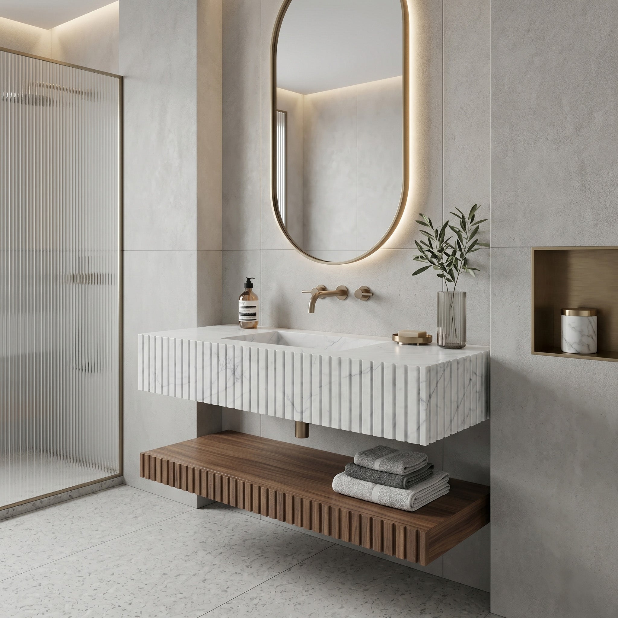 Warm minimalist bathroom interior featuring a fluted White Carrara marble single sink, a floating fluted walnut wood shelf, an oval backlit mirror, soft grey concrete walls, and a reeded glass shower screen.