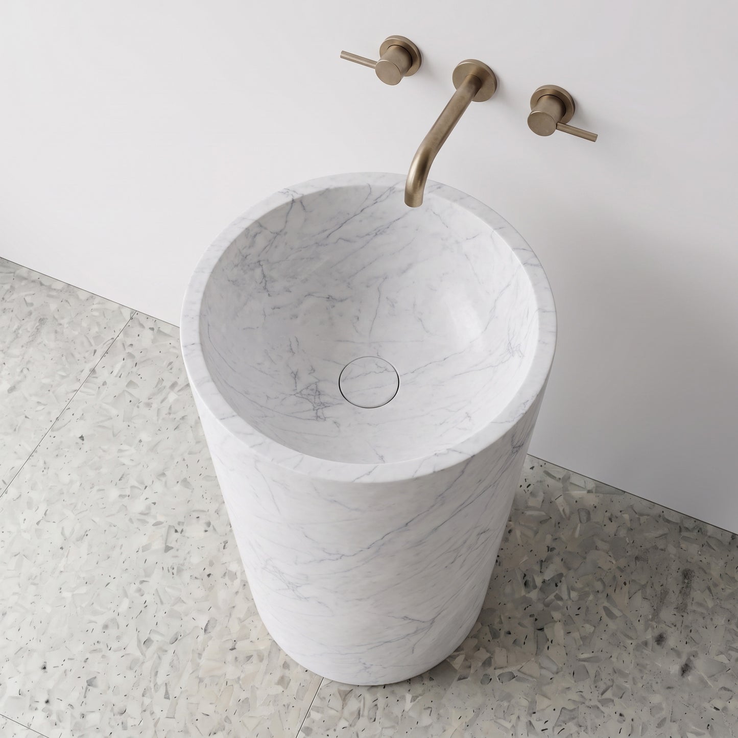 High-angle top view of a White Carrara cylindrical marble pedestal sink showing soft grey veining and matching integrated carved stone drain cap.