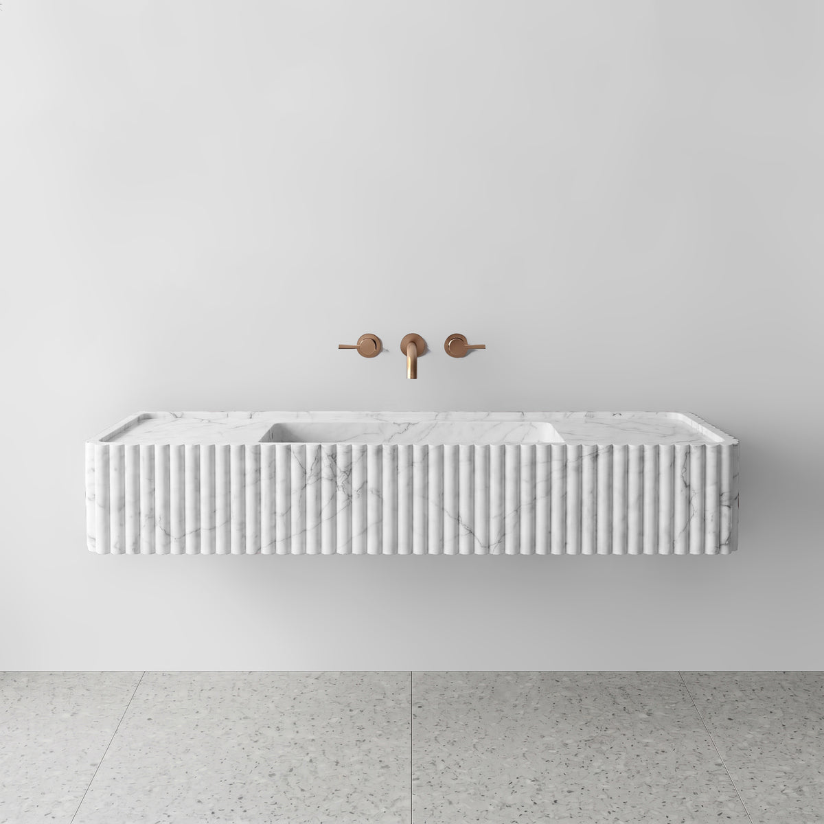 Front view of the White Carrara marble fluted monolith sink showing subtle grey veining across the vertical convex ribbed apron and wall-mounted brushed bronze faucet.