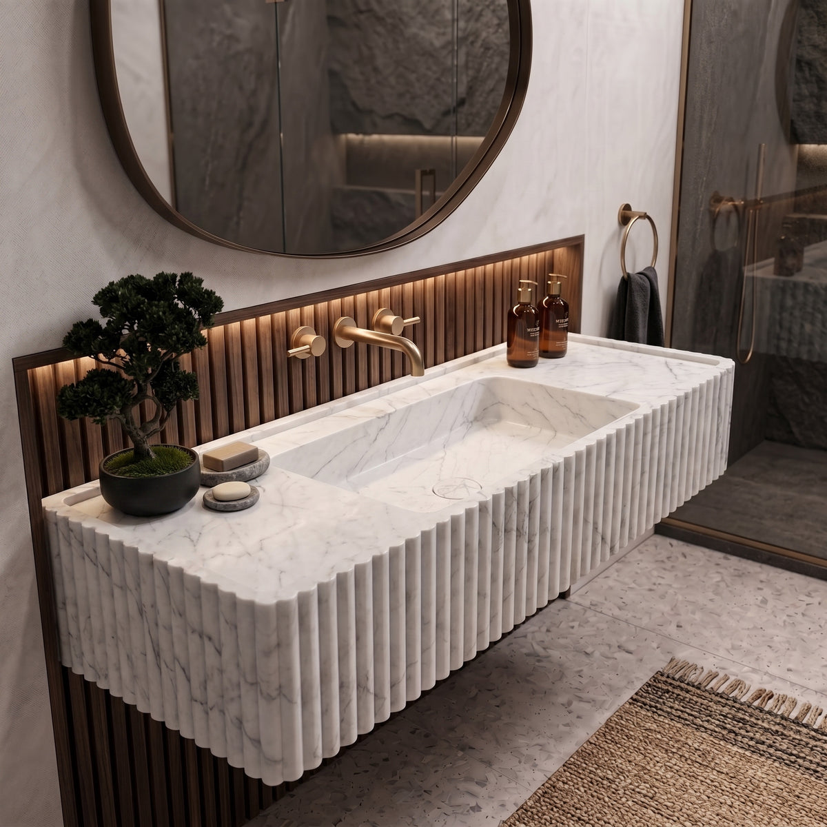 Modern luxury bathroom interior featuring the floating White Carrara fluted stone sink set against illuminated slatted walnut wood panels, a round mirror, and a bonsai accent.